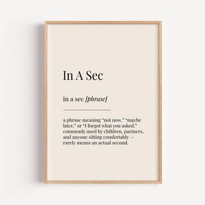 May include: A printable wall art print with a beige background and black text. The text reads "In A Sec" and defines the phrase "in a sec" as meaning "not now", "maybe later", or "I forgot what you asked". It also states that the phrase is commonly used by children, partners, and anyone sitting comfortably, and rarely means an actual second.