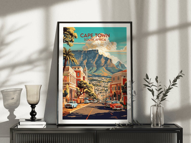 May include: A vintage-style travel poster featuring a colorful illustration of Cape Town, South Africa. The poster depicts a cityscape with buildings, palm trees, and a mountain in the background. The text "CAPE TOWN SOUTH AFRICA" is displayed at the top of the poster.
