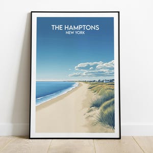 May include: Framed art print featuring a coastal scene of The Hamptons, New York. The artwork depicts a sandy beach, blue ocean, and a clear sky with clouds. The text "THE HAMPTONS NEW YORK" is displayed at the top.
