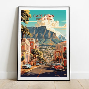 May include: A vintage-style travel poster featuring a colorful illustration of Cape Town, South Africa. The poster depicts a street lined with buildings, palm trees, and cars, with Table Mountain in the background.