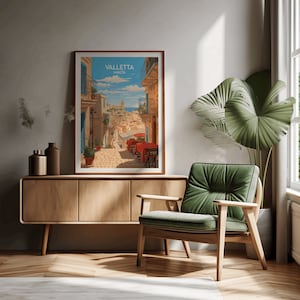 May include: A framed poster with a vintage travel illustration of Valletta, Malta. The poster features a colorful depiction of a narrow street with buildings, a blue sky, and a red-roofed building in the distance. The text "Valletta Malta" is printed in white on a blue background.