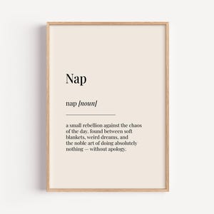 Può includere: Una stampa incorniciata con la definizione di "Nap". Il testo è nero su sfondo crema, con una cornice in legno. La definizione recita: "una piccola ribellione contro il caos della giornata, trovata tra morbide coperte, sogni strani e la nobile arte di non fare assolutamente nulla - senza scuse."