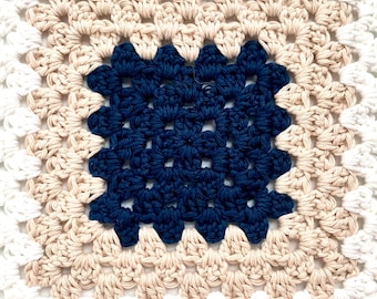 May include: A crocheted square with a white border, a beige center, and a dark blue center square.
