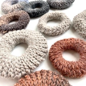 May include: A collection of knitted rings in various colors and textures, including gray, brown, and beige. The rings are all crocheted and have a unique, handmade look.