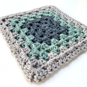 May include: A crocheted square with a gray border and a center made of green and gray yarn.
