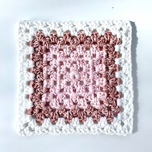 Peut inclure: Un carré crocheté avec un dégradé de rose et de brun. Le carré est entouré d'une bordure blanche.
