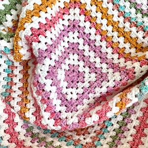 May include: A crocheted blanket with a white background and colourful stripes in shades of pink, orange, green, and blue.