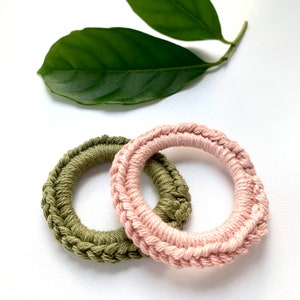 May include: Two crocheted rings, one in a light green color and the other in a light pink color. The rings are interlocked.