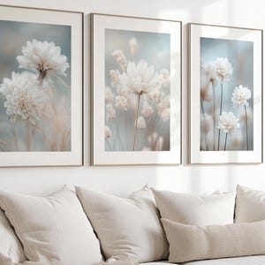 Puede incluir: Tres impresiones enmarcadas de delicadas flores blancas con un fondo suave y borroso. Las impresiones están dispuestas en una fila en una pared blanca.