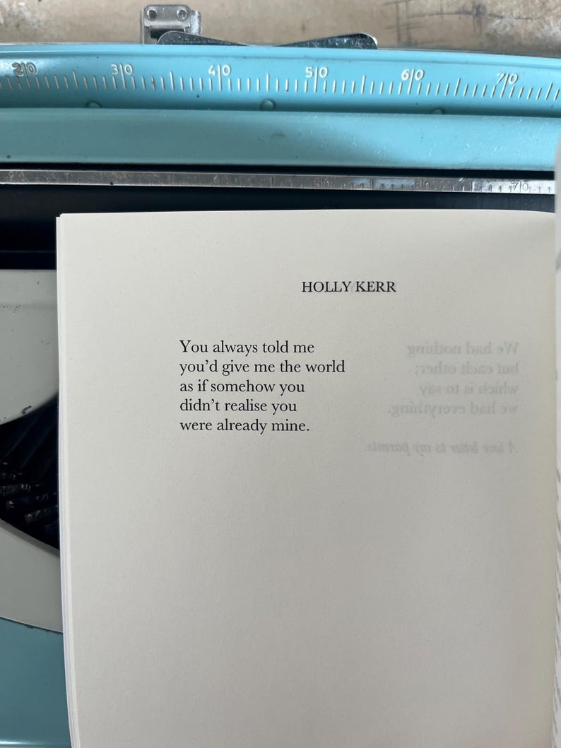 Puede incluir: P&aacute;gina de libro con el texto "You always told me you'd give me the world as if somehow you didn't realise you were already mine." de HOLLY KERR. Una m&aacute;quina de escribir azul vintage en el fondo, creando un ambiente nost&aacute;lgico.