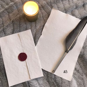 May include: A white envelope with a red wax seal and a white sheet of paper with a feather pen and the text "A5" on a gray fuzzy surface.
