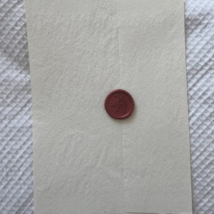May include: A white envelope with a red wax seal featuring a floral design.