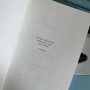 Puede incluir: Un libro abierto con el texto: "Para aquellos que crecieron pensando que nunca ser&iacute;an escuchados. Te escucho." El libro est&aacute; abierto en una p&aacute;gina blanca, con una m&aacute;quina de escribir azul en el fondo.