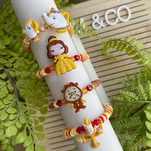 May include: Set of four beaded bracelets featuring characters from Beauty and the Beast. The bracelets are made with red, yellow, and white beads and feature charms of Belle, the Beast, Mrs. Potts, and Lumiere.