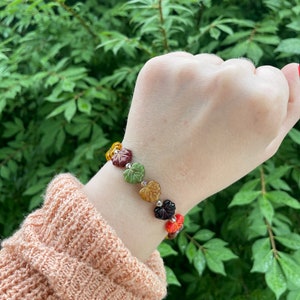Op de afbeelding: Een armband met glazen blad kralen in tinten oranje, groen, bruin en rood. De armband wordt gedragen op een pols.
