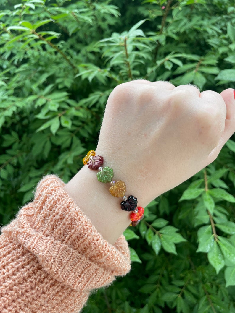 Op de afbeelding: Een armband met glazen blad kralen in tinten oranje, groen, bruin en rood. De armband wordt gedragen op een pols.