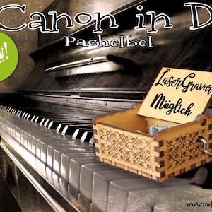 Op de afbeelding: Een houten muziekdoos met een bloemmotief speelt het lied "Canon in D" van Pachelbel. De muziekdoos is open en het deksel is opengeklapt. Het deksel heeft de tekst "Laser Gravier Möglich" erop. De muziekdoos staat op een zwart pianoklavier. Een groene cirkel met het woord "Nieuw!" staat in de linkerbovenhoek van de afbeelding.