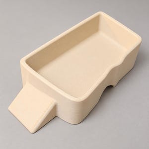 May include: A rectangular, cream-colored tray with a smooth, matte finish. The tray features a raised, solid base with a distinct, angled ramp-like extension on one side and a curved, indented cutout along the center of one of the longer side walls.