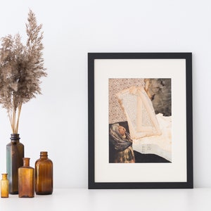 May include: A framed artwork with a black border, featuring a collage of vintage paper and a sepia-toned image. Beside it, a collection of amber glass bottles and a vase with dried ornamental grass. The composition evokes a rustic, bohemian aesthetic.