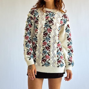 Puede incluir: Una taza de cerámica blanca con un asa negra y el texto "But first, coffee" en un estilo manuscrito. La taza está sobre una superficie blanca. La taza es probablemente para bebidas calientes.