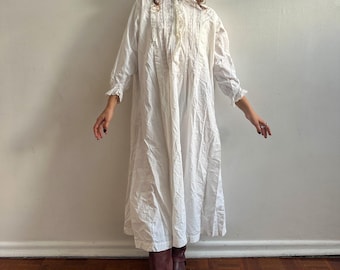May include: A white cotton nightgown with lace trim and a button-up front. The gown has a long, flowing skirt and is worn with brown boots.