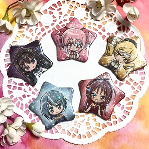 May include: Five star-shaped buttons with different anime characters on each. The characters are all girls with different colored hair and outfits. The buttons are on a white doily with a pink and orange background.