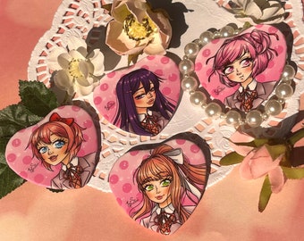 May include: Four pink heart-shaped buttons with different anime characters. Each button has a white polka dot pattern. The buttons are on a white doily with pink flowers.