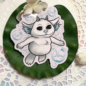 Puede incluir: Una pegatina blanca con un personaje de dibujos animados con detalles azules, cuernos pequeños y orejas grandes. La pegatina tiene burbujas de texto que dicen "Sippin", "Straight" y "Chlorine". La pegatina está sobre una hoja verde.