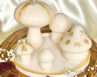 May include: Set of four white mushroom-shaped candles with gold glitter accents. The candles are arranged on a wooden slice with a white rim.