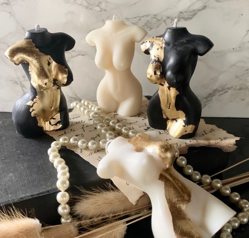 Puede incluir: Tres velas decorativas con forma de torso humano. Cada vela est&aacute; pintada de negro o blanco con detalles dorados. Las velas est&aacute;n dispuestas sobre una superficie con una cadena de perlas.