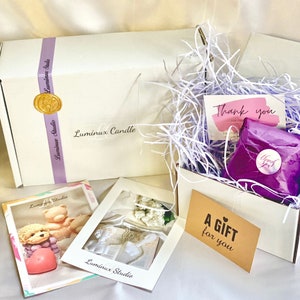Op de afbeelding: Een witte cadeaudoos gevuld met wit geribbeld papier, een paarse cadeauzak met een bedankje-sticker, een kaart met de tekst "Een cadeau voor jou" en een kaart met de tekst "Bedankt".