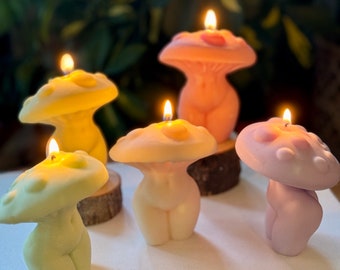 May include: Five mushroom-shaped candles with a human figure design. The candles are in various colors, including pink, yellow, and purple.