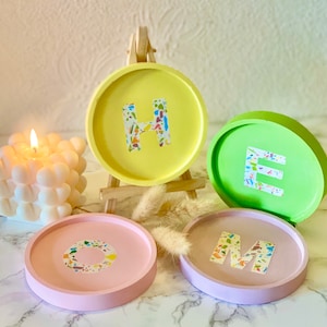 Puede incluir: Cuatro posavasos coloridos con las letras "HOME" escritas en blanco con un patrón de confeti colorido. Los posavasos están hechos de un material rosa claro, amarillo, verde y morado claro.