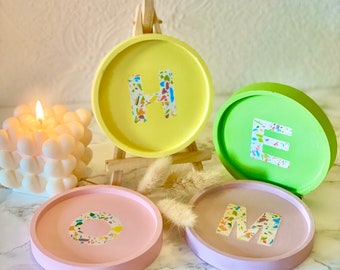 Puede incluir: Cuatro posavasos coloridos con las letras "HOME" escritas en blanco con un patrón de confeti colorido. Los posavasos están hechos de un material rosa claro, amarillo, verde y morado claro.