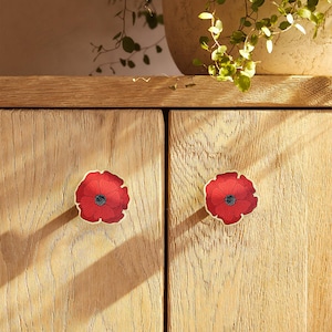 Może przedstawiać: Dwie drewniane drzwiczki szafki z czerwonymi gałkami w kształcie maków. Drzwiczki szafki są jasne, z widocznym usłojeniem drewna.