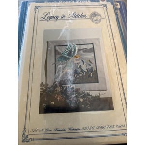 May include: A cross-stitch kit titled "Legacy in Stitches" featuring a fairy with butterfly wings. The kit includes a framed design with a fairy in a flowing gown, surrounded by flowers. The address 720 N. Grom, Kennewick, Washington 99336, (509) 783-7804 is printed on the bottom.
