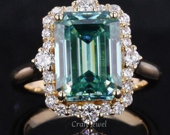 Emerald-Cut Green Moissanite Engagement Ring Yellow Gold And Surrounded by a Halo of Smaller Diamond Reflecting Elegantly On a Dark Surface