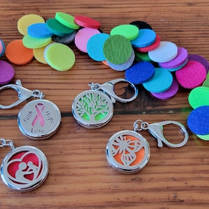 May include: Three silver keychains with different designs. Each keychain has a round, clear glass locket with a metal design inside. The lockets are surrounded by a silver ring with a metal hook. The lockets are labeled "Faith, Hope, Love", "Tree of Life", and "Butterfly". The keychains are surrounded by a variety of colorful felt circles.