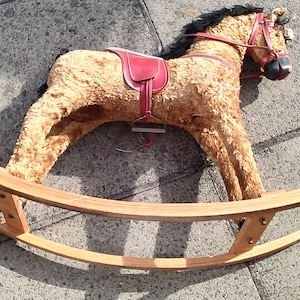 May include: A vintage rocking horse toy made of brown plush with a red saddle and a black mane and tail. The horse is on a wooden rocking base.