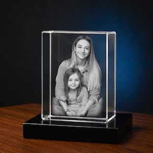 May include: A clear, rectangular crystal photo block featuring a monochrome image of a woman and a child. The block is set on a black, glossy base, against a dark backdrop.