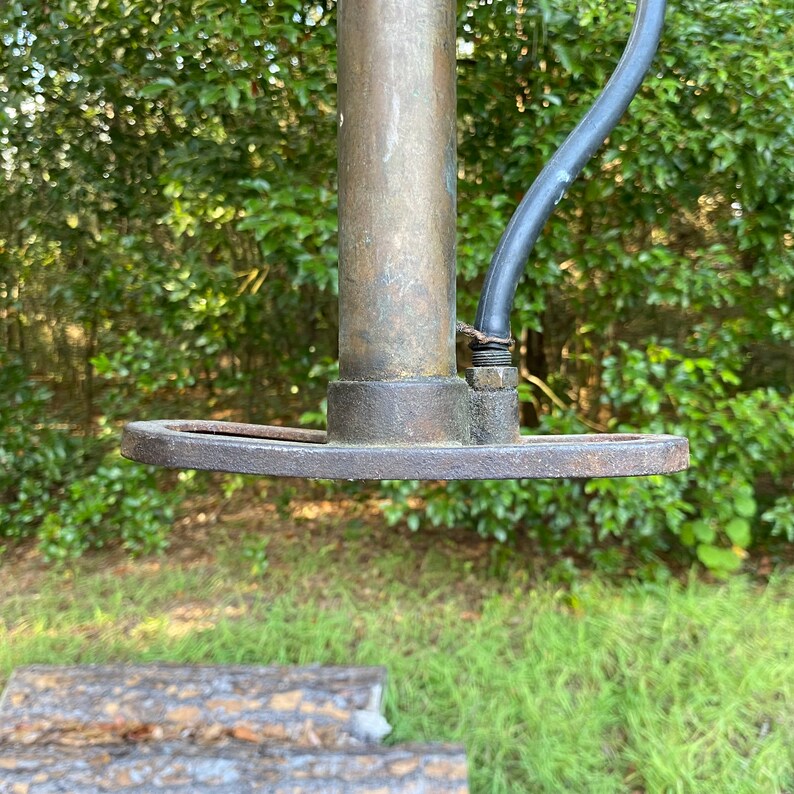 Puede incluir: Primer plano de una bomba de bicicleta vintage de lat&oacute;n con una manguera de goma negra. La bomba tiene una base de metal con un borde redondeado.