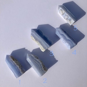 May include: Five blue agate crystal points, arranged in a diagonal line on a white surface. The points are all different sizes and shapes, and they have a variety of blue and white patterns.