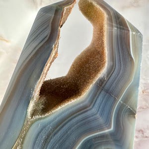 May include: A large, natural agate crystal with a unique, open, cave-like formation. The crystal is a light blue and brown color with a smooth, polished surface.