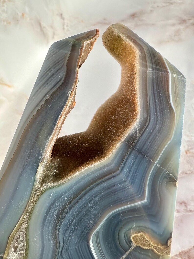 May include: A large, natural agate crystal with a unique, open, cave-like formation. The crystal is a light blue and brown color with a smooth, polished surface.