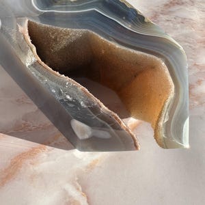 May include: A large, gray and brown agate geode with a natural opening. The geode has a smooth, polished surface and intricate banding patterns.