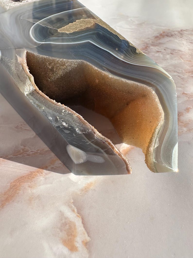 May include: A large, gray and brown agate geode with a natural opening. The geode has a smooth, polished surface and intricate banding patterns.