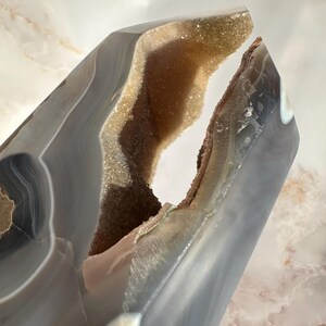 May include: A large, gray agate geode with a natural opening revealing a sparkling, light brown crystal interior. The geode has a smooth, polished exterior and a unique, irregular shape.