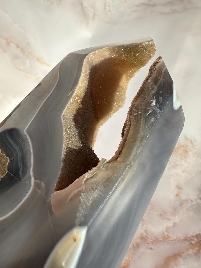 May include: A large, gray agate geode with a natural opening revealing a sparkling, light brown crystal interior. The geode has a smooth, polished exterior and a unique, irregular shape.