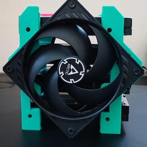 Puede incluir: Un ventilador de ordenador negro con cuatro aspas curvas, montado en un marco negro cuadrado. El ventilador tiene un logotipo blanco y negro en el centro. El ventilador está sujeto por soportes de color verde brillante.