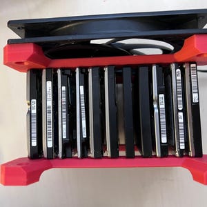 Puede incluir: Un bastidor de discos duros de impresión 3D de color rojo con un ventilador negro en la parte superior. El bastidor contiene 10 discos duros, cada uno con un número de serie único.